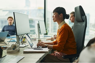 Woman in an office, sitting at a desk looking at a compueter screen with other coworkes sitting beside her