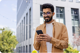 Man standing outdoors looking down at a phone that she's holding in his hand