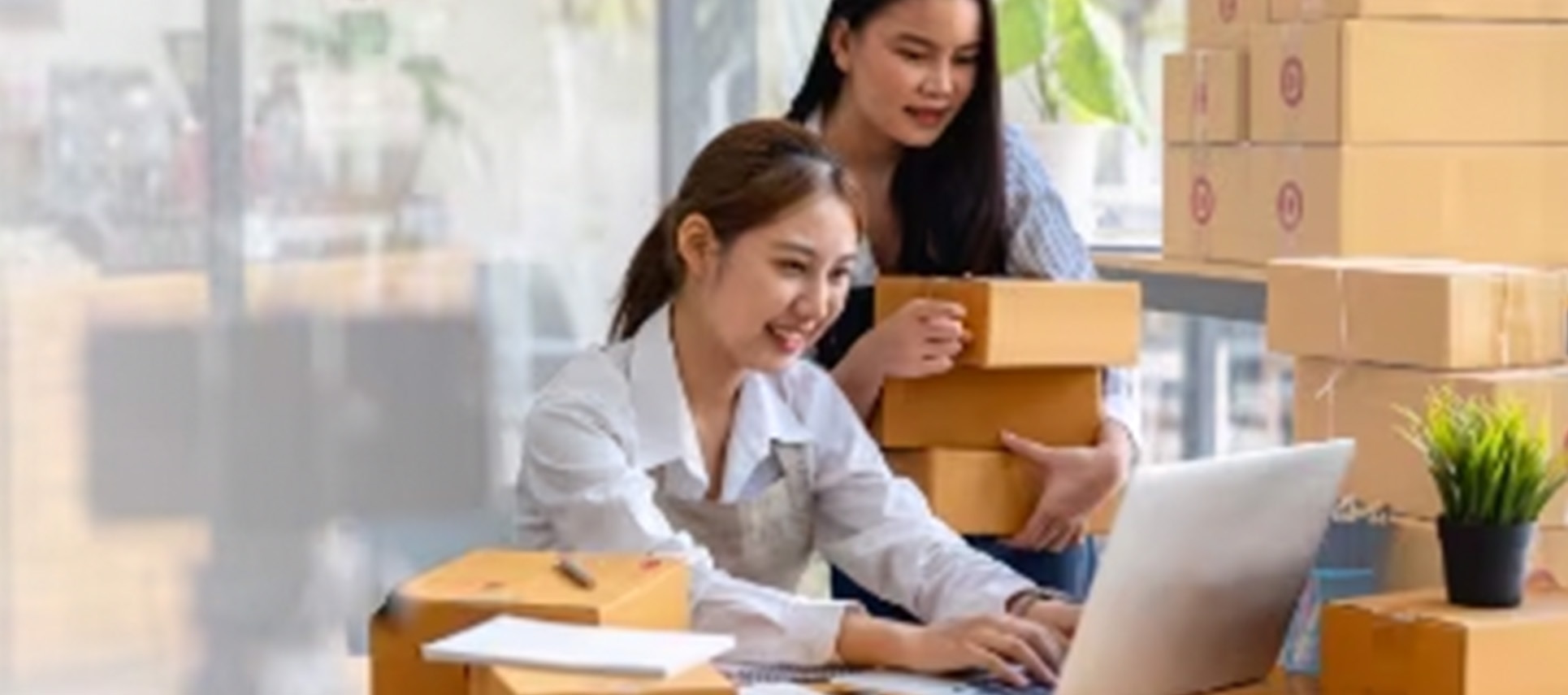 Two women working with laptop and shipping boxes at desk