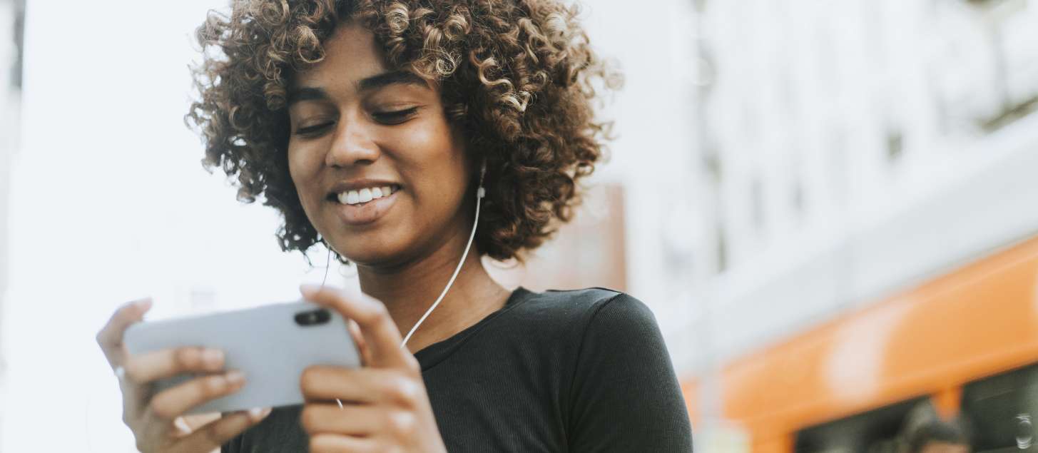 Woman holding a cell phone with wired earbuds.