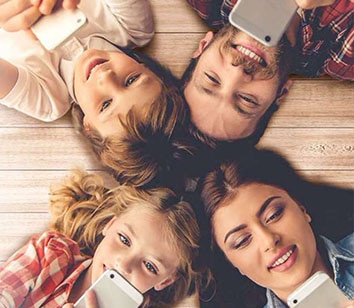 A family of four, who are Spectrum Mobile customers, laying on the floor using cell phones.
