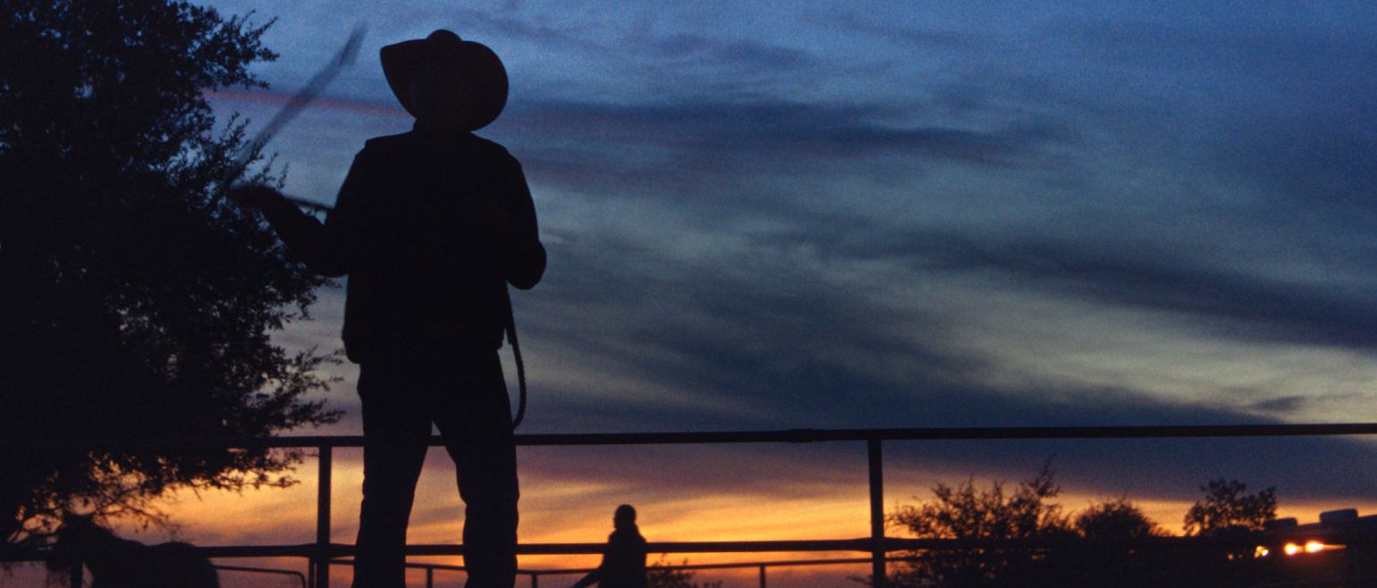 A silhouette of a rancher in front of a sunset. 