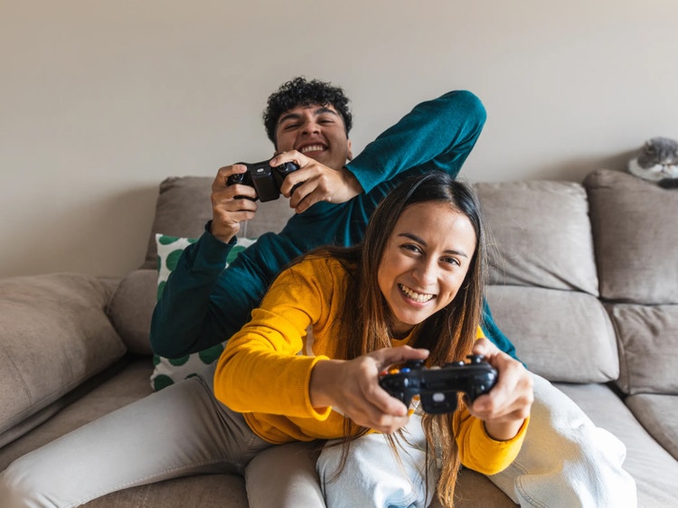 Dos personas se divierten jugando videojuegos en un sofá.