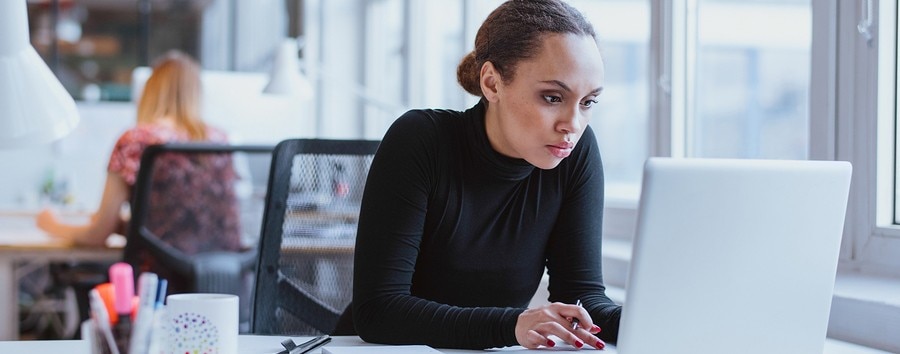 Business woman sitting at a desk in an office working on a laptop.
