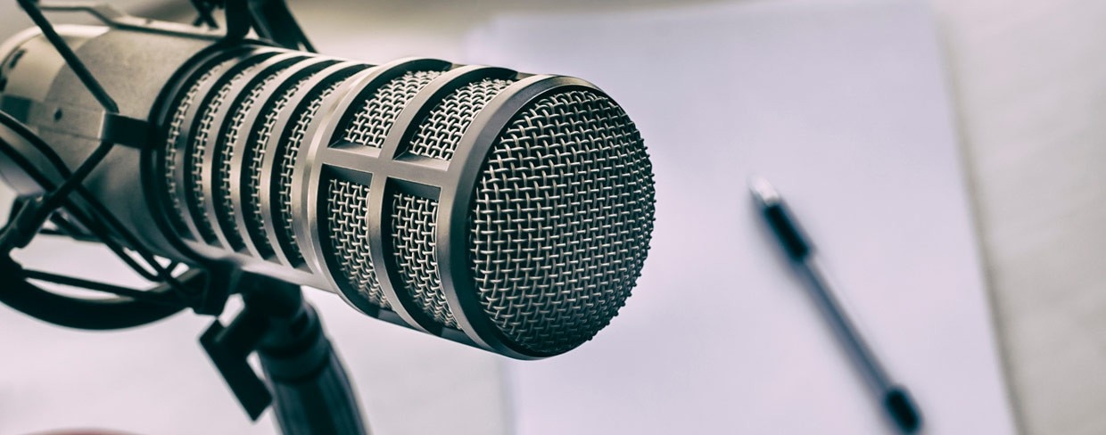 Close up of podcast microphone with pen and notepad on a desk in the background