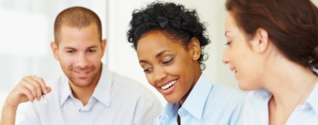  Two businesswomen and a businessman smile while having a conversation at work.