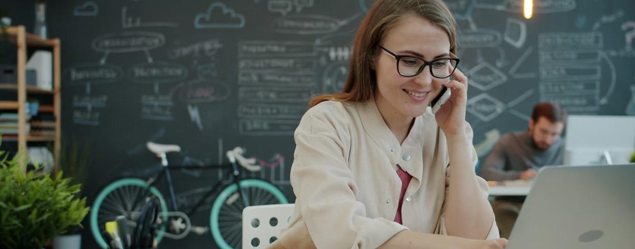 Woman talking on phone while working on laptop in office