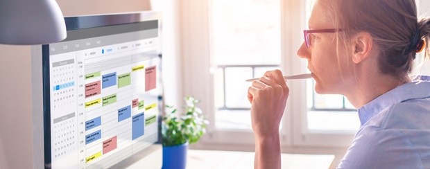 A businessperson looks intently at a computer screen showing a work calendar.