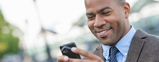 Professional man in business attire smiling while looking at his smartphone outdoors