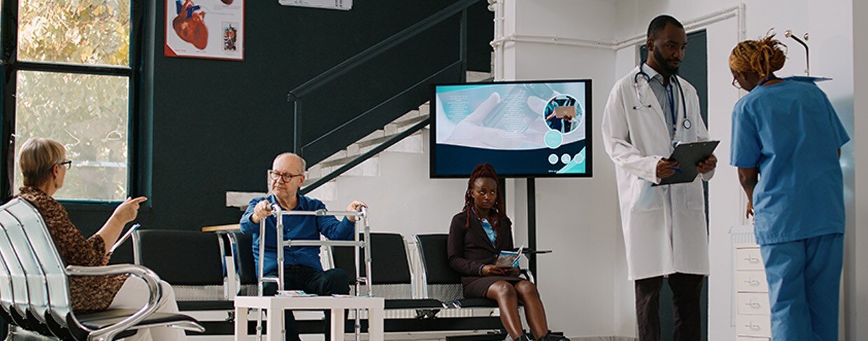 Patients waiting in a modern medical clinic lobby while a doctor reviews a tablet with a nurse.