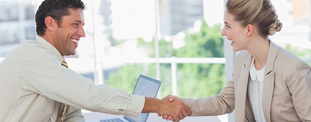 Business man cheerfully shakes the hand of a business woman, while they both smile.