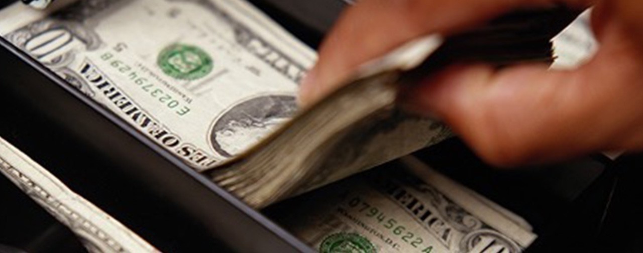 Hand grabbing a stack of $10 bills from a register.