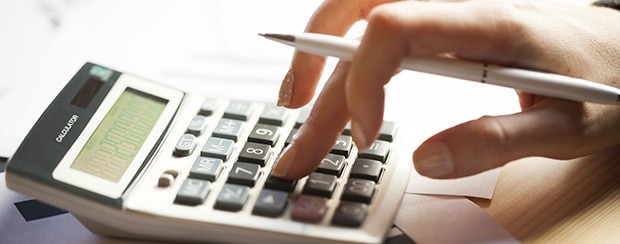Hand uses a calculator on a desk, while also holding a pen, as a person makes calculations.