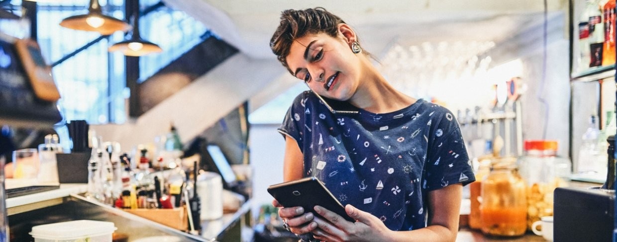Bartender uses a tablet while also on the phone using a smart phone