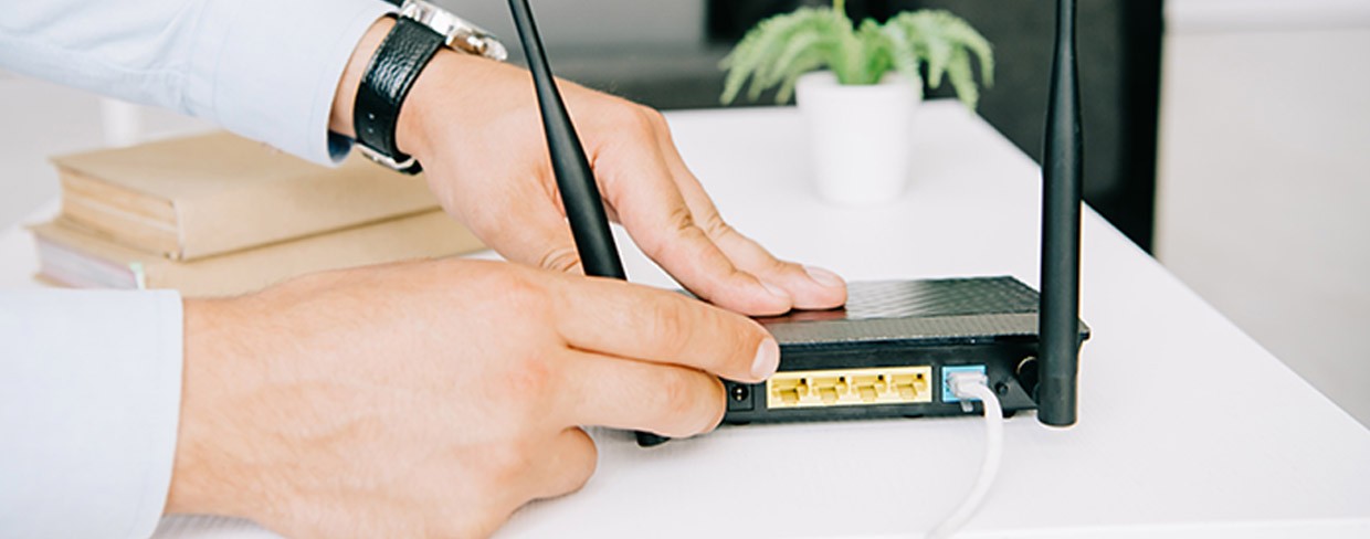 Close-up of a person adjusting a wireless internet router with two antennas on a white desk.