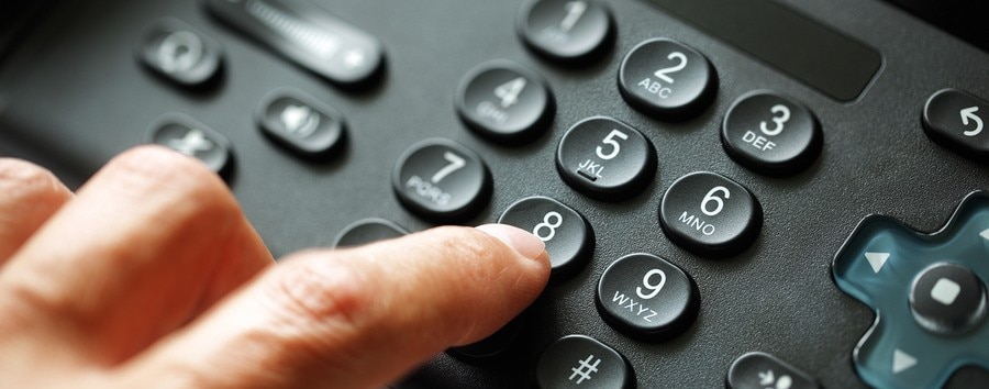 VoIP desk phone with hand touching keypad on a modern office desk