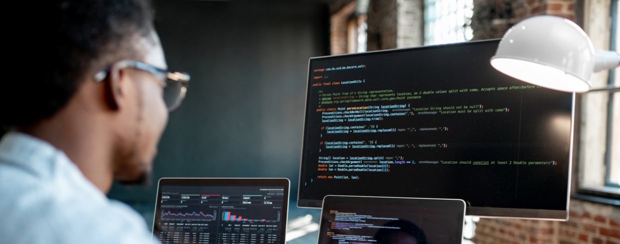 Developer looking at code on monitor and two laptops.