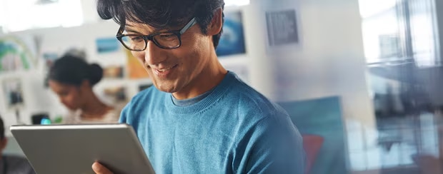 Business man wearing glasses uses a tablet in an office setting.