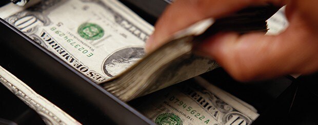 Hand grabbing a stack of $10 bills from a cash register.