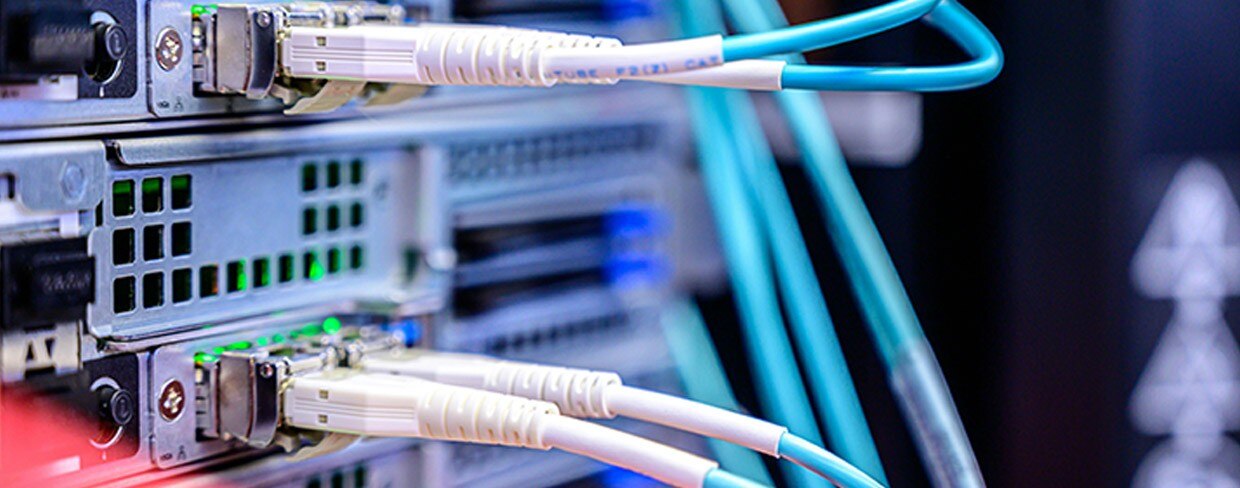 High-speed Ethernet and fiber-optic cables plugged into a server rack in a data center with LED network lights