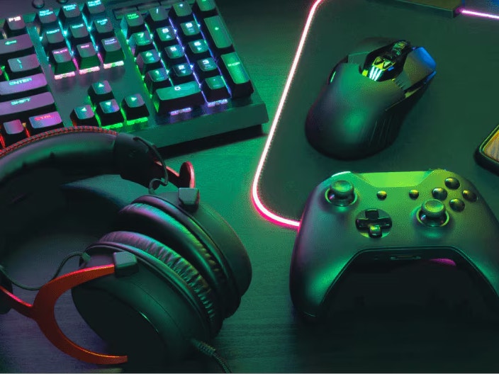 Gaming equipment such as keyboards, headphones, controlars and a mouse on a dark desktop