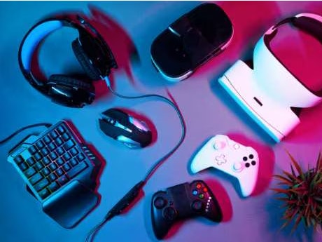 Gaming devices laying on a table, including headphones, controlers, and keyboards.