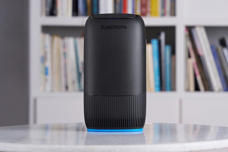 Un enrutador Spectrum negro está sobre una mesa frente a una estantería.