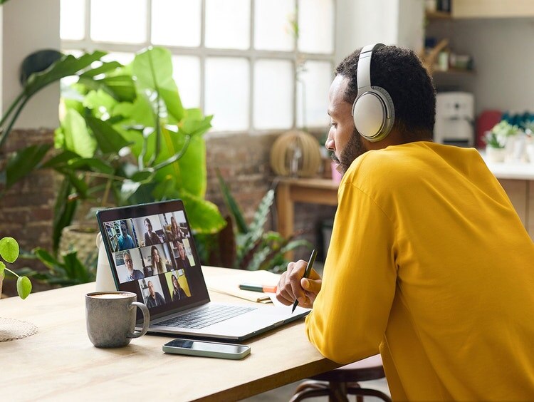 Un hombre con auriculares se sienta a la mesa y se une a una videollamada en su laptop.