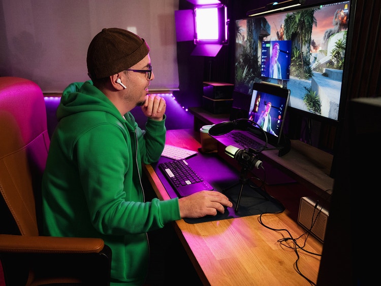 Una persona con una sudadera con capucha verde juega en una computadora con varias pantallas.