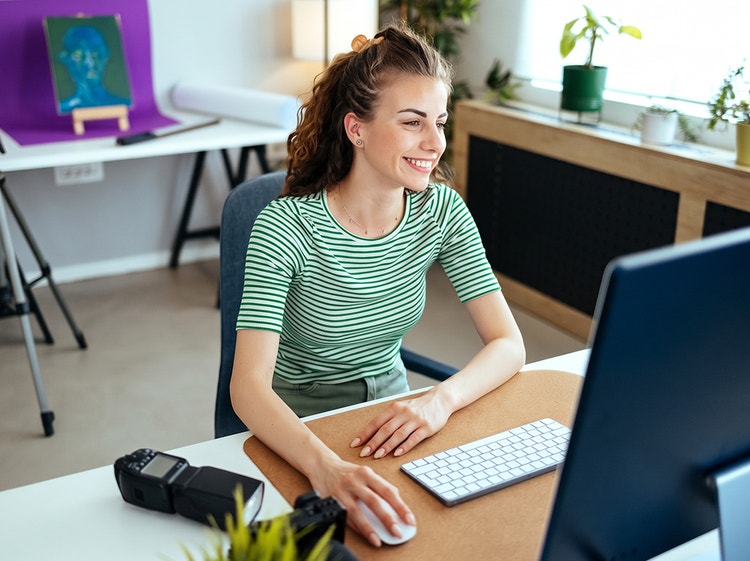 Una mujer sonriente está sentada en un escritorio trabajando en una computadora en una oficina en casa.