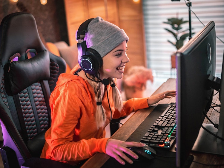 Una persona con una sudadera con capucha rosa y auriculares juega un videojuego en una silla para juegos.