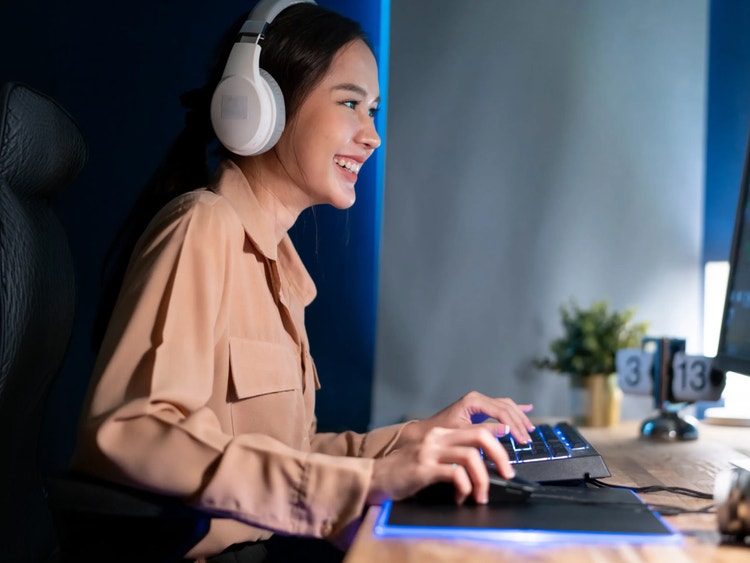 Una mujer sonriente con auriculares escribe en un teclado en una habitación iluminada de azul.