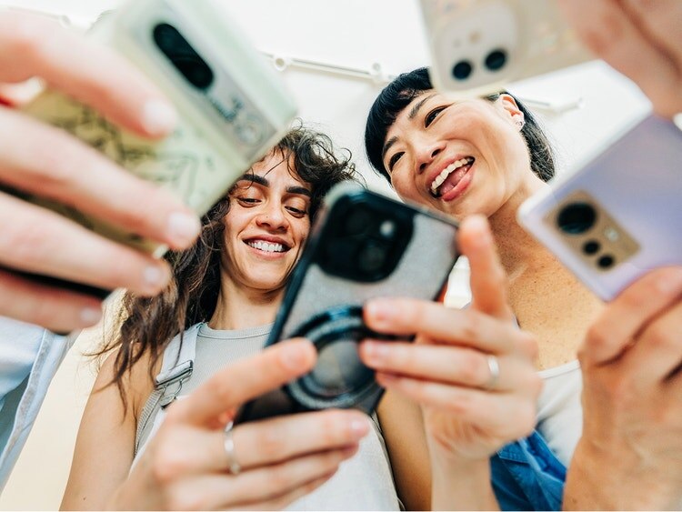 Tres amigos sonríen y sostienen sus teléfonos hacia la cámara.