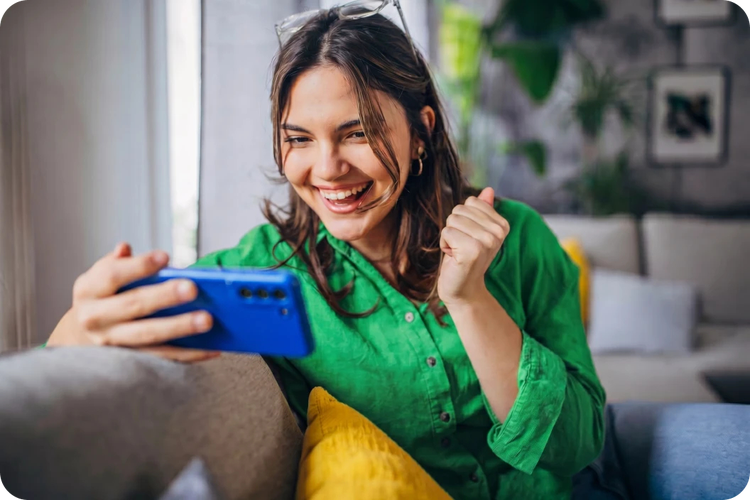 Woman in a green top holding her phone and raising her fist in a celebratory gesture.