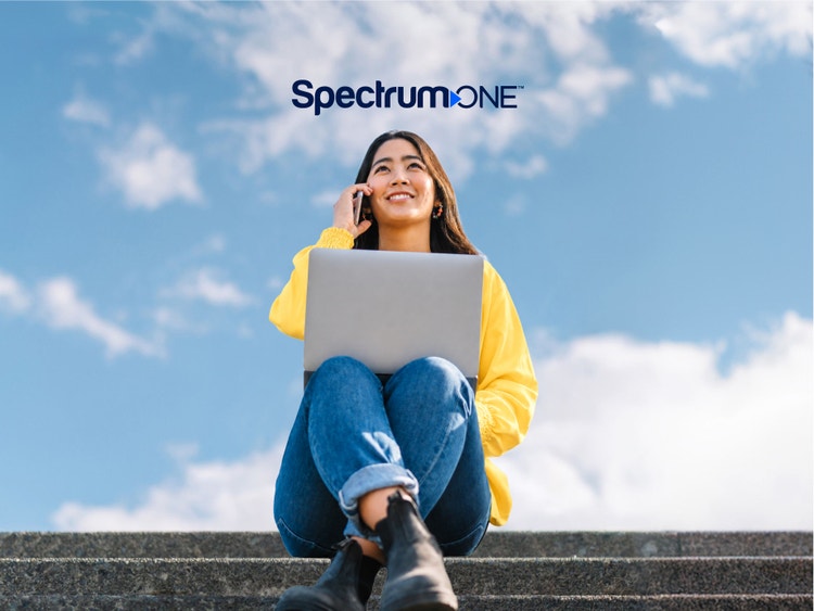 Happy woman using laptop and mobile device outdoors with the Spectrum One logo
