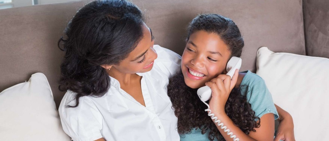 Happy girl on a home phone sitting next to her mom.