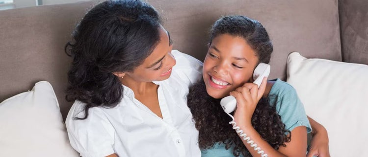 Niña contenta hablando por un teléfono residencial, sentada junto a su madre.