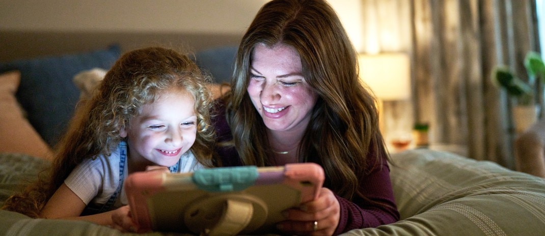 A woman and a girl sharing a tablet, smiling.