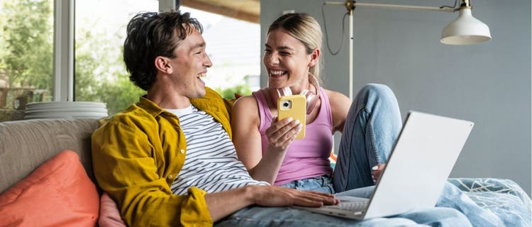 Man and woman looking at each other smiling holding phone and laptop
