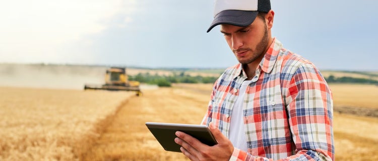 Man using Spectrum Internet on a tablet in a field with a harvesting machine in the background.