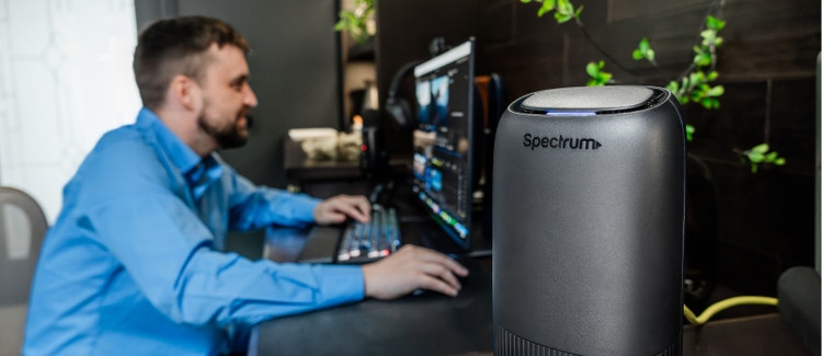 Man at desk using computer with a Spectrum internet router nearby