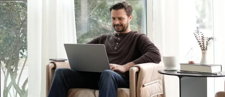 Hombre sonriente con un teléfono móvil y una laptop mientras trabaja desde casa
