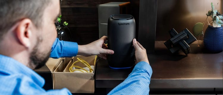 Man self-installing a Spectrum modem at home, box and cable beside him.