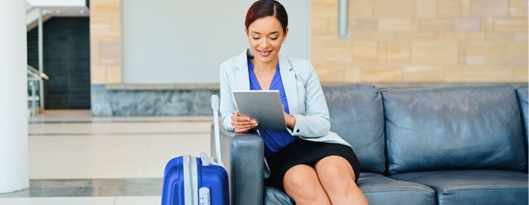 Woman looking at tablet on couch with suitcase