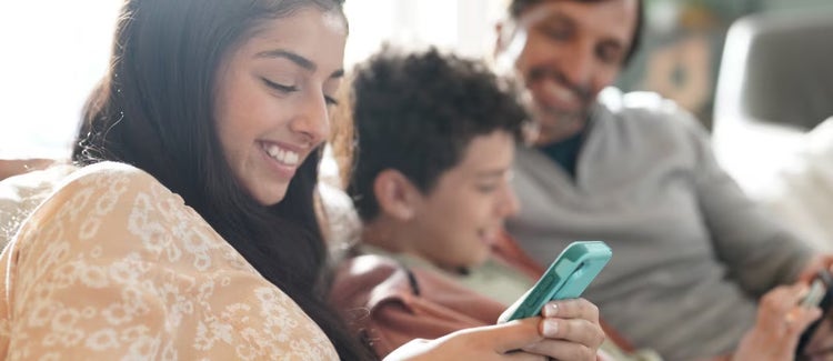 Una familia pasando el rato en el sofá. La madre está mirando su teléfono, sonriendo.