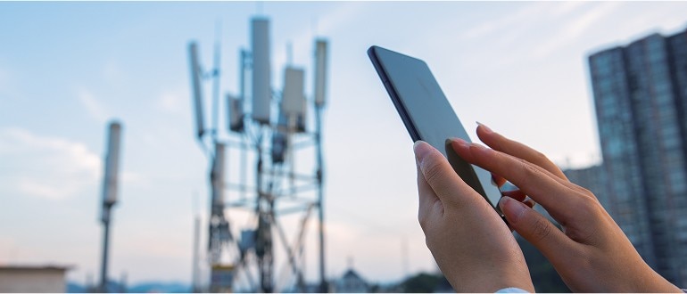 Una persona sosteniendo un smartphone frente a una torre de telefonía móvil