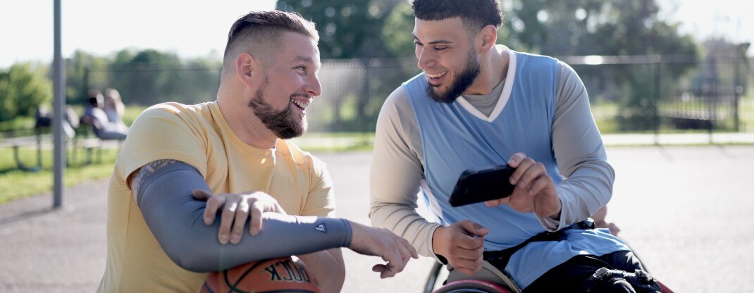 Two men smiling at each other as one shows the other something on his phone.