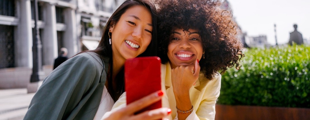 Dos mujeres posando frente a un teléfono para una foto, sonriendo.