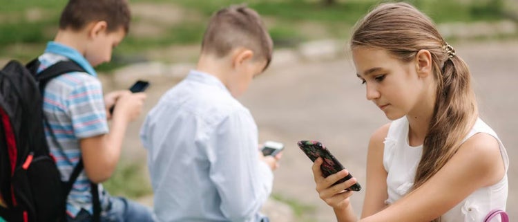Dos niños y una niña usando teléfonos móviles.
