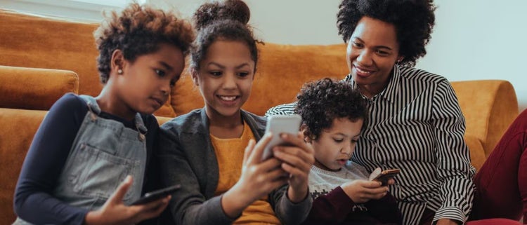 Mujer contenta con 3 niños usando teléfonos celulares.